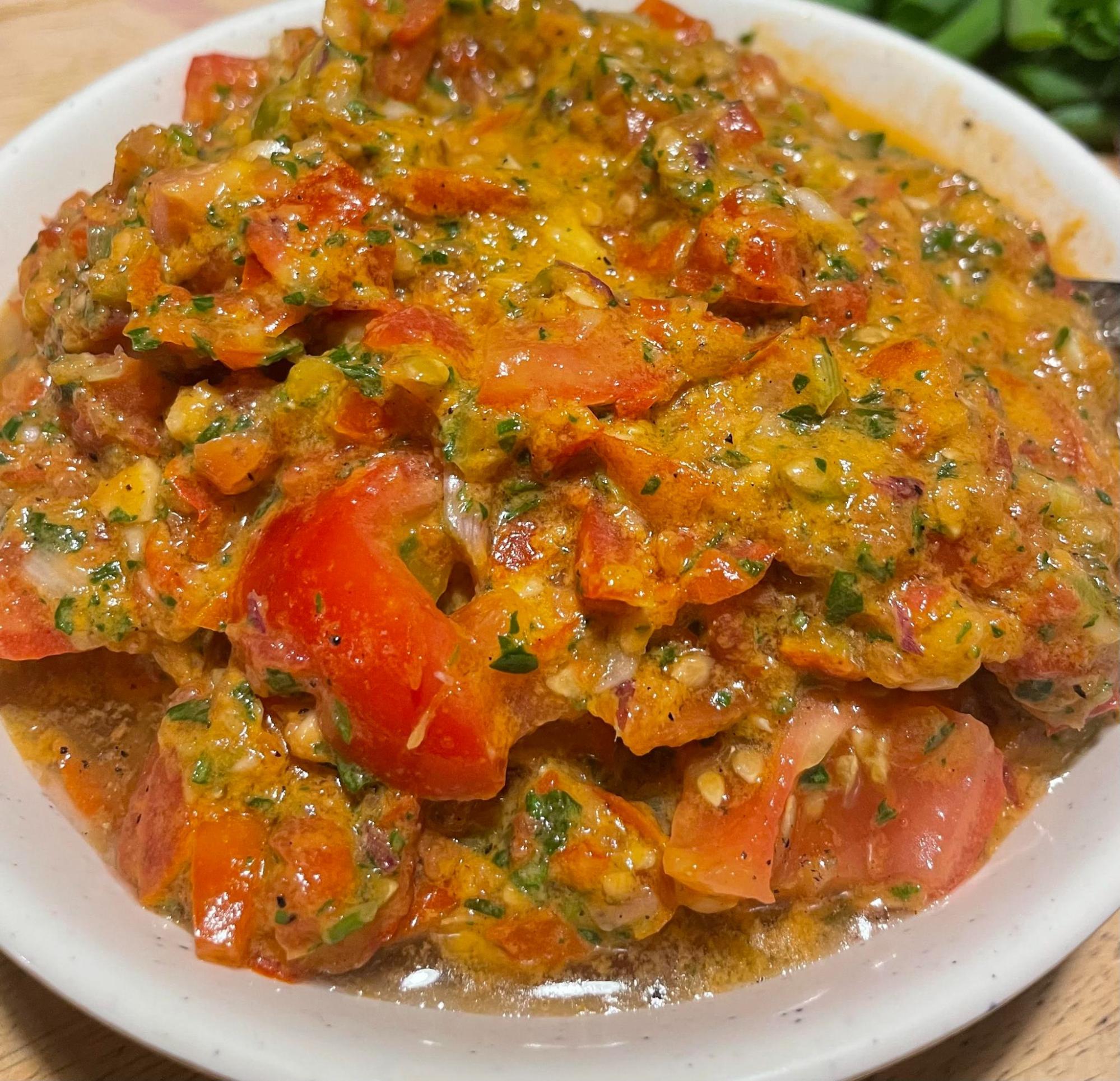 A white bowl on a tan cutting board holding the pomodoro sauce which is composed of chunks of brilliantly red tomatoes mixed with bits of white scallion, chopped green onions and bright green basil speckled throughout. The top right corner has a small peek of the green onions set on the same tan board.